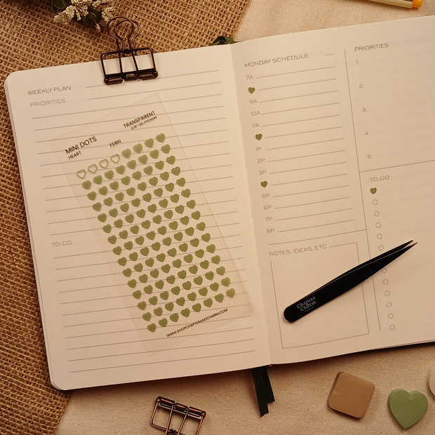 Transparent fern green heart planner sticker sheet with 120 miniature matte stickers displayed on an open weekly planner beside black tweezers, showing the product ready for planning and journaling.