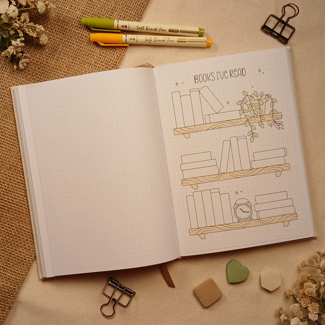 Open A5 dotted journal featuring the Books I've Read stick-in page with three decorative bookshelf illustrations, stacked books, a trailing plant, and a vintage clock. Designed to help readers create a beautiful visual record of the books they've finished while complementing any bullet journal or reading journal.