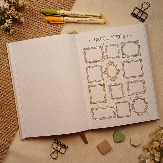 Open A5 dotted journal featuring a color Favorite Moments stick-in page with ornate vintage-style frames in soft earth tones for displaying photos, cherished memories, and keepsakes. Styled with brush pens, binder clips, dried florals, burlap, and neutral sticky notes.