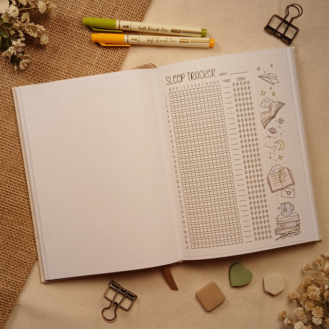 Open A5 dotted journal featuring the Sleep Tracker stick-in page with a monthly sleep log, hourly tracking grid, energy tracker, and whimsical book-themed illustrations. Designed to simplify monthly habit tracking while adding a cozy, literary touch to your bullet journal, planner, or wellness journal.