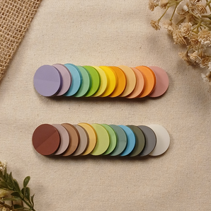 Two rows of transparent round sticky notes arranged to showcase all 24 color options on a neutral linen background with dried florals.